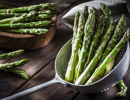 A bunch of asparagus in a steamer pan, with more on a cutting board.