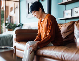 A woman seated on a couch massages her knee with both hands.