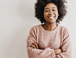 A smiling woman with folded arms in front of a light gray wall.